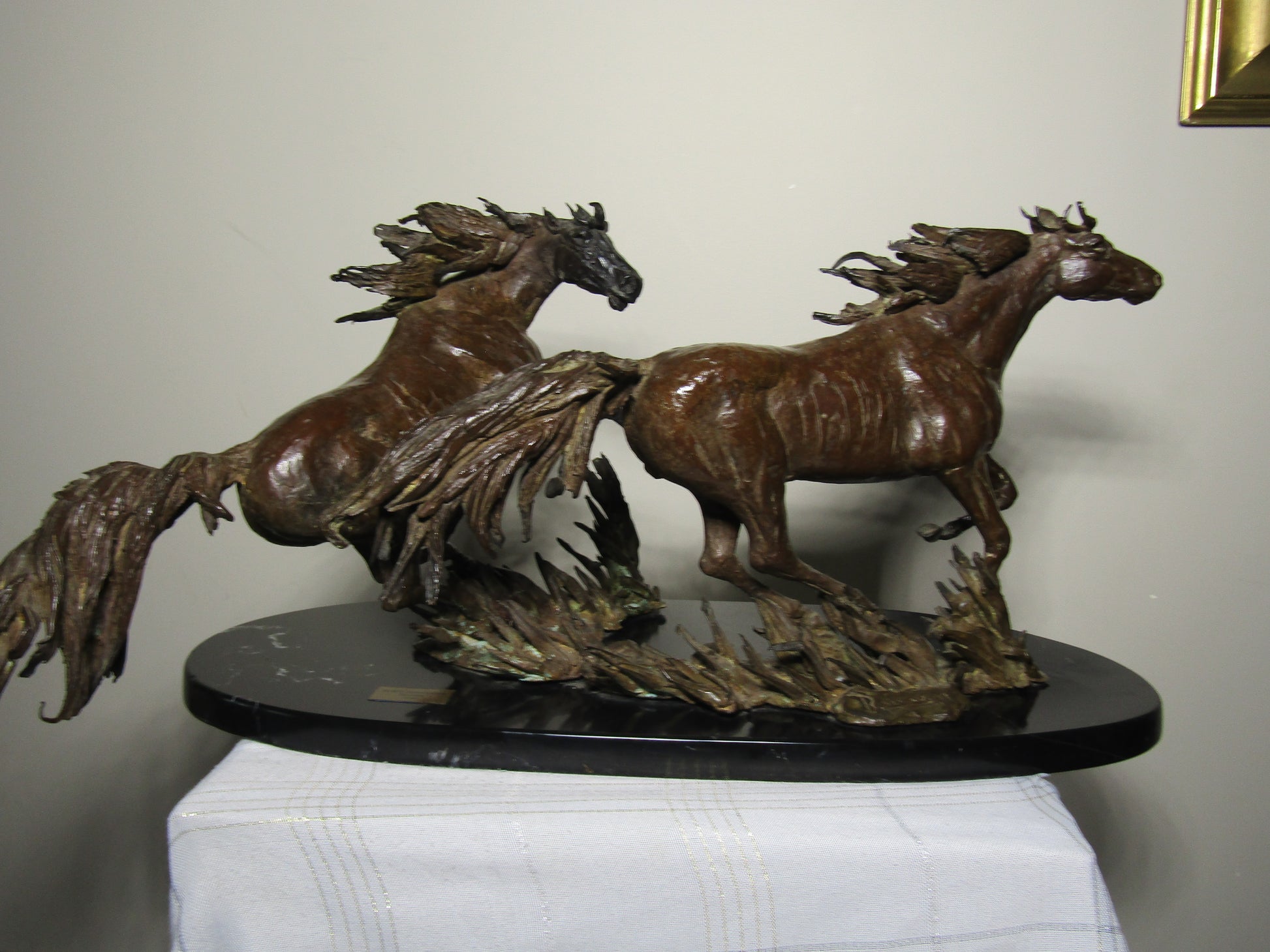Bronze sculpture of two horses on a black base against a plain background