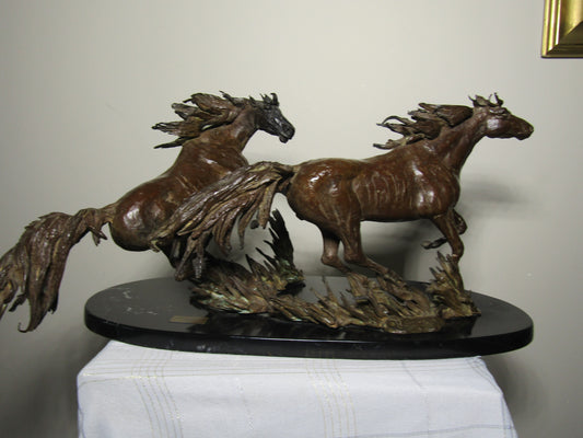Bronze sculpture of two horses on a black base against a plain background